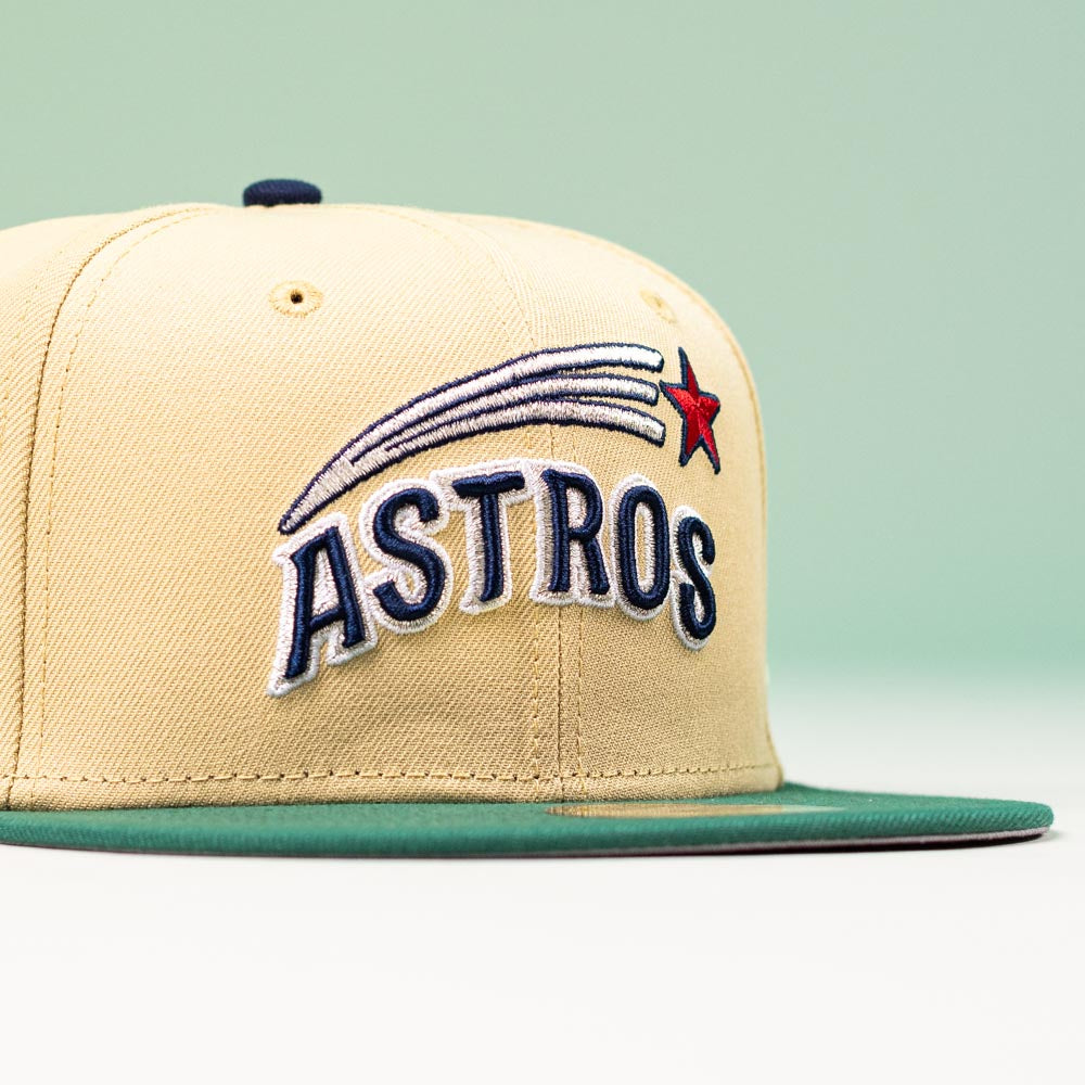 The New Era Hat 5950 Houston Astros Vegas Gold Emerald Aeros 5950 Day features ASTROS in blue, a red star, white shooting star streaks on the front, an Astrodome sidepatch, a tan crown, and a green flat brim with a light green background.
