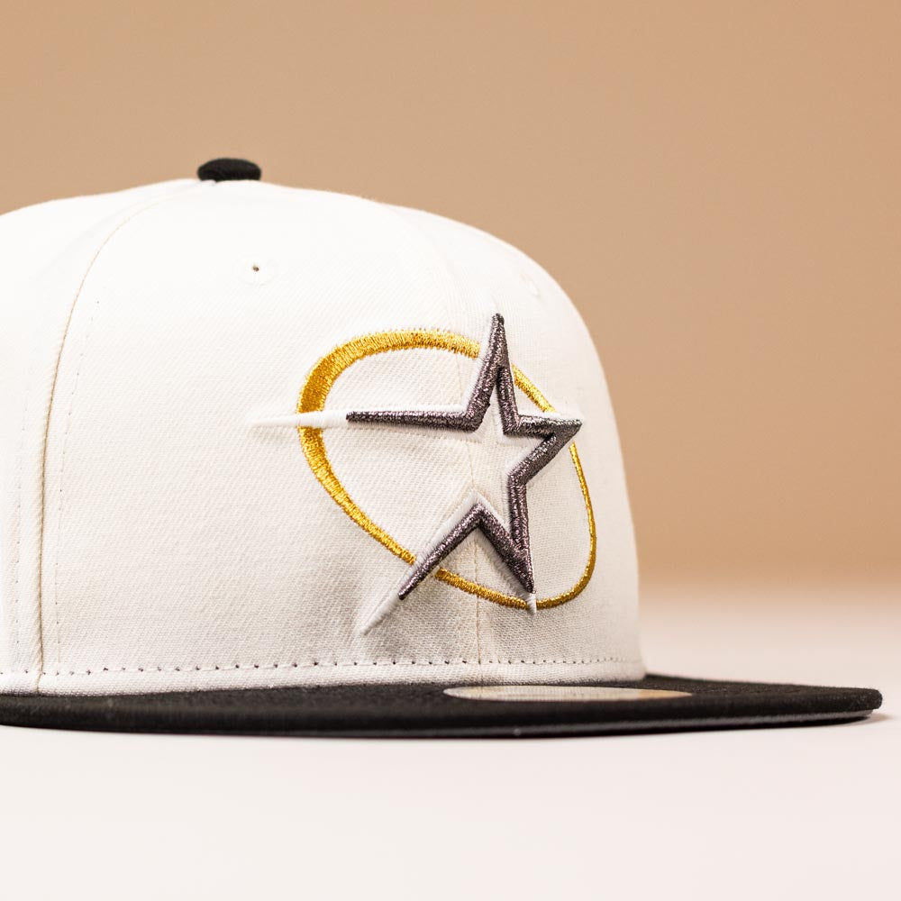 A White Black Circle Star Houston Astros New Era 5950 Fitted hat with a black brim and embroidered gold and silver star on the front, photographed against a light beige background.
