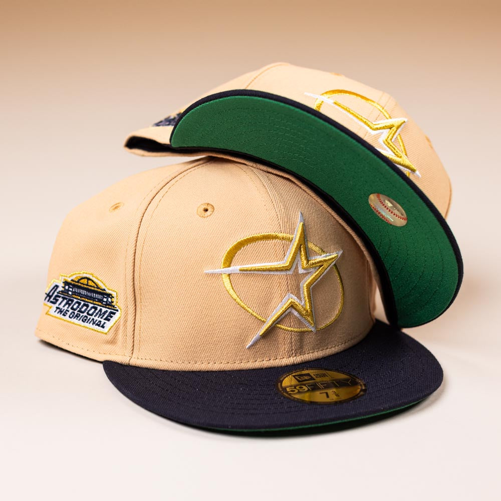 Two tan and black New Era 5950 fitted Houston Astros hats are stacked, each with a circle star logo and "The Original" Astrodome patch. One visor faces up, displaying its sticker—true standout pieces from 5950 Day.