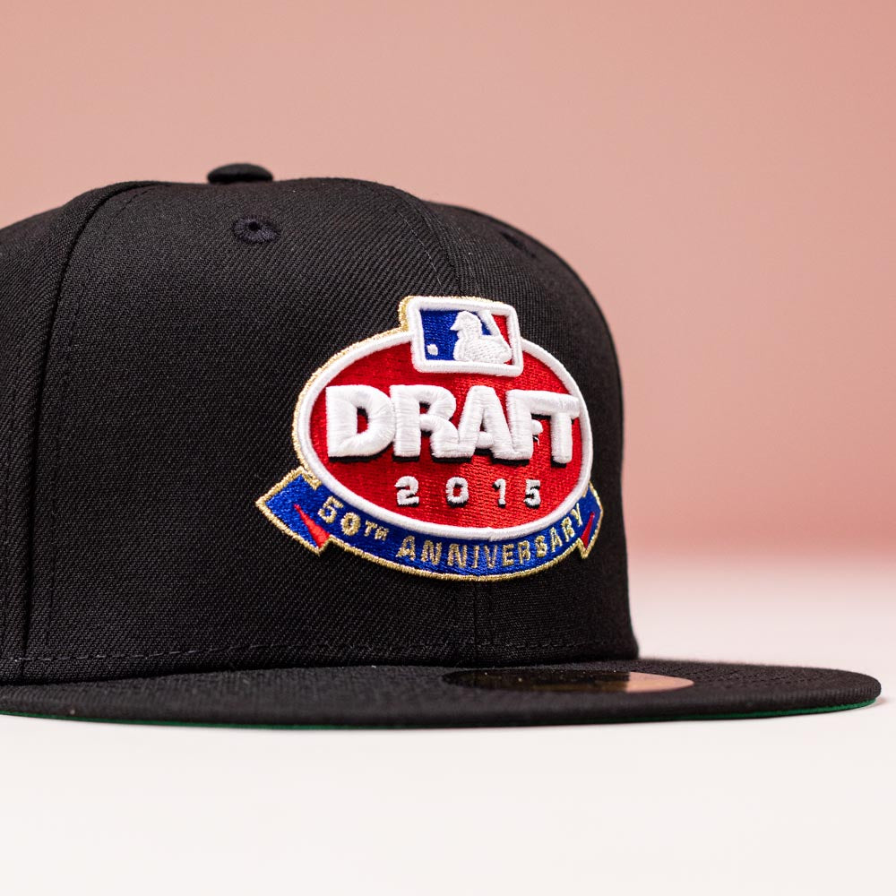 The Throwback 2015 Draft Day Black Red Blue Houston Astros New Era 5950 Fitted Hat features a large MLB Draft 50th Anniversary embroidered patch, displayed on a plain pink background.