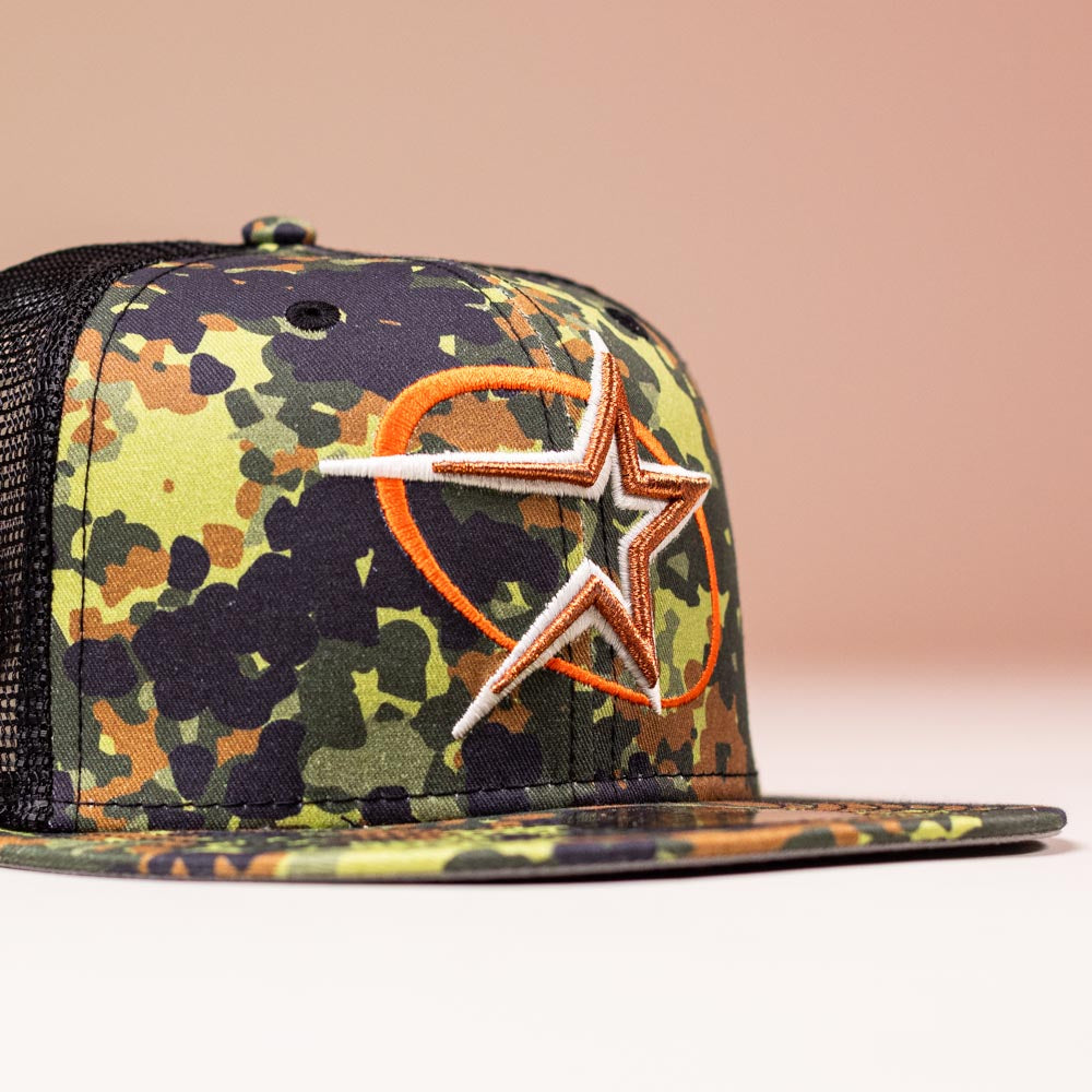 The Fleck Black True Houston Astros New Era 5950 Fitted Hat features a camouflage pattern, black mesh back, and an orange-outlined star logo embroidered on the front, set against a solid light beige background.