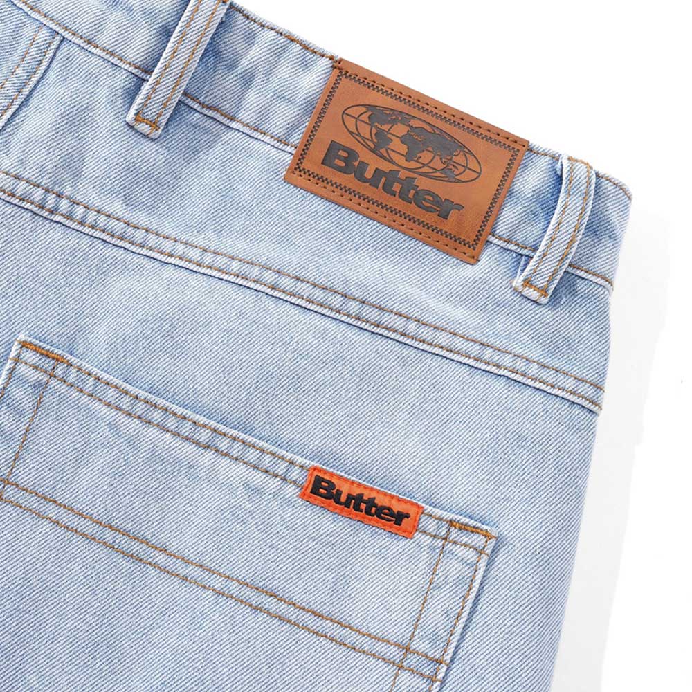 Baggy Light Blue Denim Jeans by Butter Goods in 100% cotton feature a brown leather patch with a globe and "Butter" on the waistband, plus an orange Butter tag on the back pocket for signature style.
