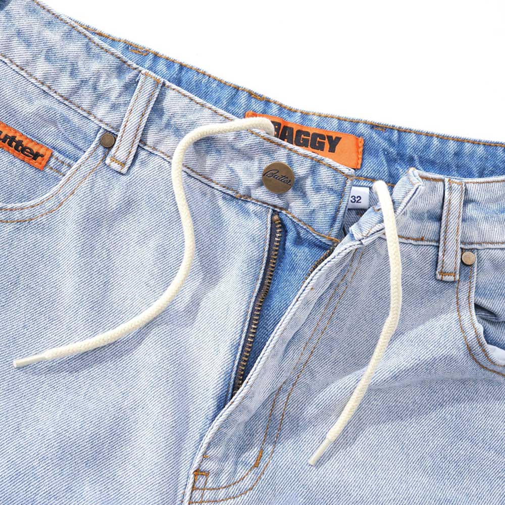 Baggy Light Blue Denim Jeans by Butter Goods feature a white drawstring, visible button, partially open zipper, orange BAGGY and 32 tags at the waistband, and an orange label near the pocket. Made from 100% cotton denim.