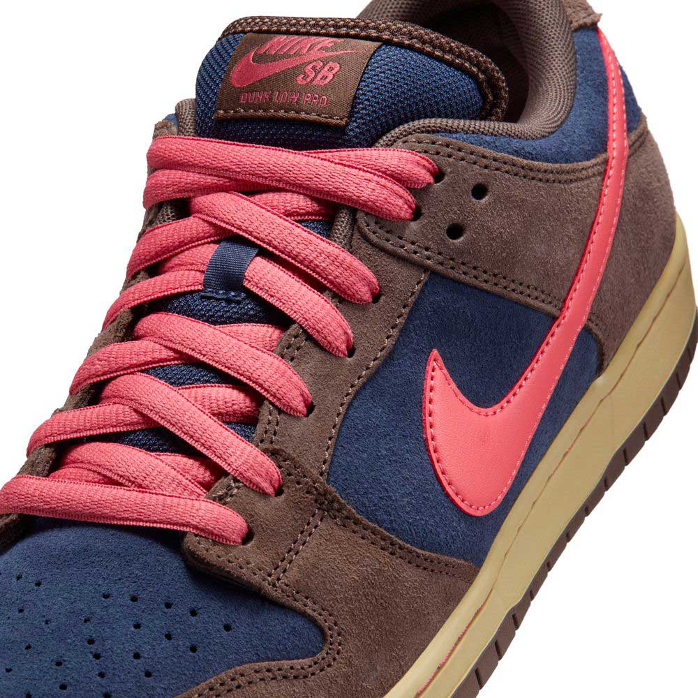 Close-up of the Baroque Brown Adobe Midnight Navy Dunk Low Pro HQ1625200 Nike SB Suede Shoes, featuring a brown suede overlay, blue base, pink Swoosh and laces, beige sole, and a brown tongue label with pink Nike SB text.