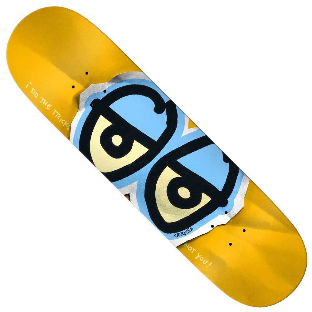The Basalt Construction DBX 8.38x32.1 Eyes Gold Krooked Skateboard Deck features a yellow design with a blue cartoon face and the phrases "I Do THE Tricks" and "Not You!", plus lightweight basalt technology for enhanced performance.