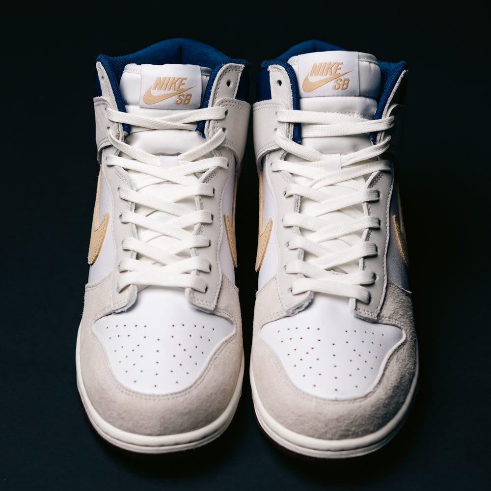 The Ivory Sand Blue Void Dunk High Pro x Beyond IU4491100 Nike SB Skateboarding Shoes feature a white and light gray upper with tan swooshes and accents, blending classic basketball sneaker heritage with modern street style, as seen from above on a dark background.