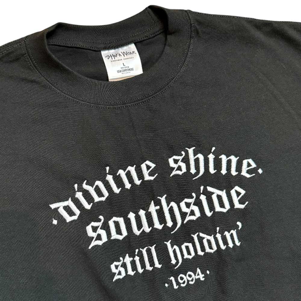 The Black Divine Shine x Southside Still Holdin Max Heavyweight Tee features white gothic embroidery with 'divine shine. southside still holdin 1994,' honoring Southside Skatepark—a bold pick for streetwear fans. Collar label displays the Divine Shine brand.