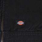 Close-up of the Thrasher Magazine x Dickies Skateboarding A88CE BLK black jacket showing adjustable cuffs, a visible brown zipper on the left, and a rectangular Dickies logo patch near the bottom center.