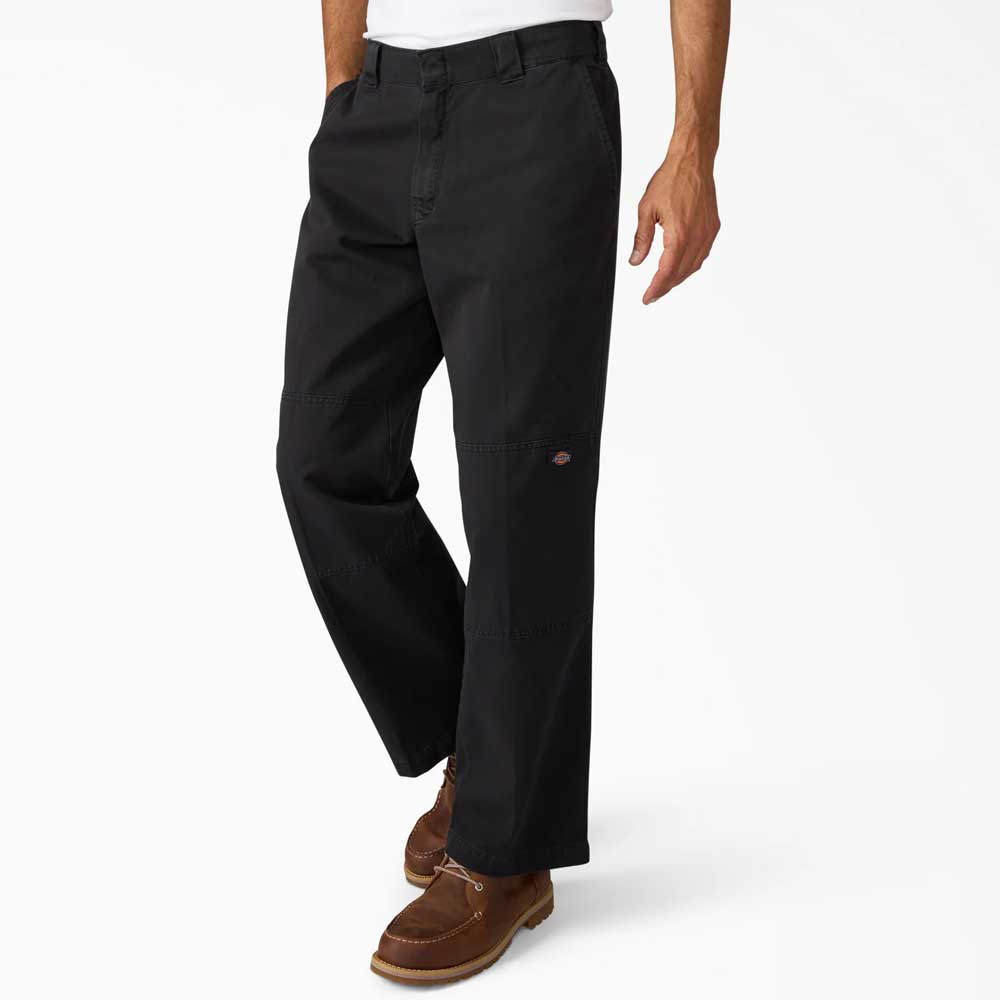A person wears the Black Worn In Double Knee Pant A89TCBLK by Dickies Skateboarding and brown leather shoes, standing with hands in pockets against a plain white background.