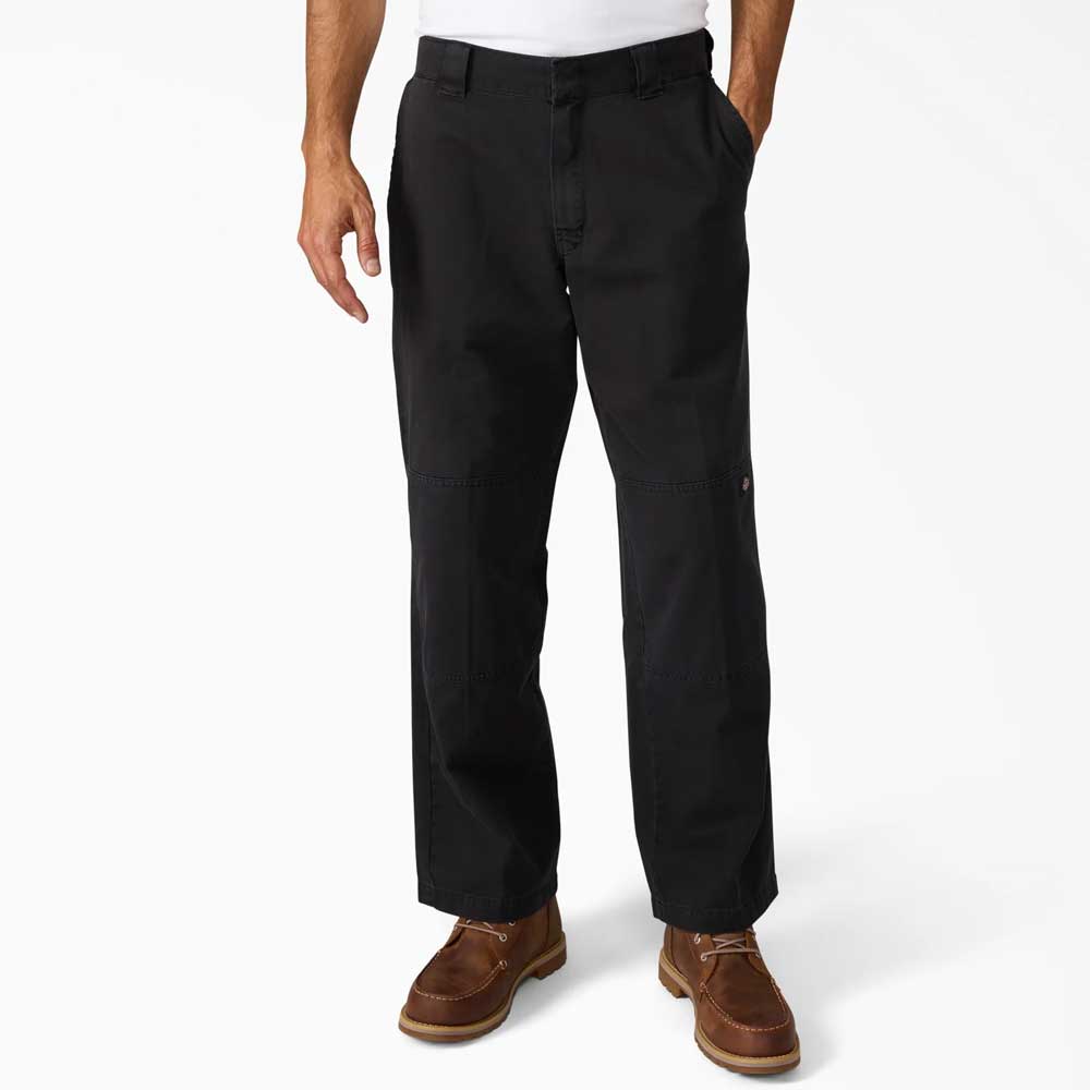 A man wearing Black Worn In Double Knee Pant A89TCBLK Dickies Skateboarding, a white 100% cotton T-shirt, and brown leather shoes stands with his hands in his pockets against a plain white background.