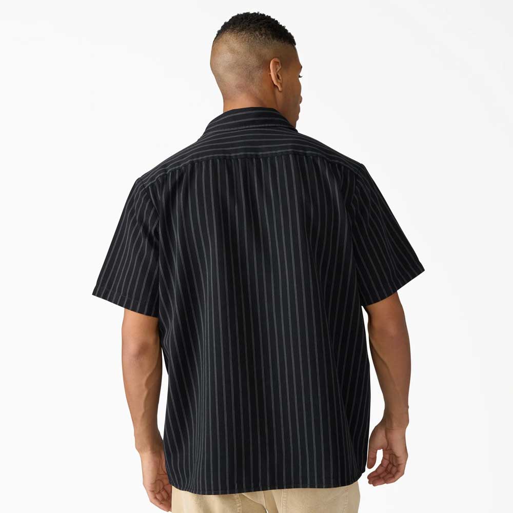 A person with short hair is seen from behind in a black Dickies Skateboarding Worn In Lightweight Work Shirt A89G7BLK with thin white stripes, paired with light pants, against a plain white background.