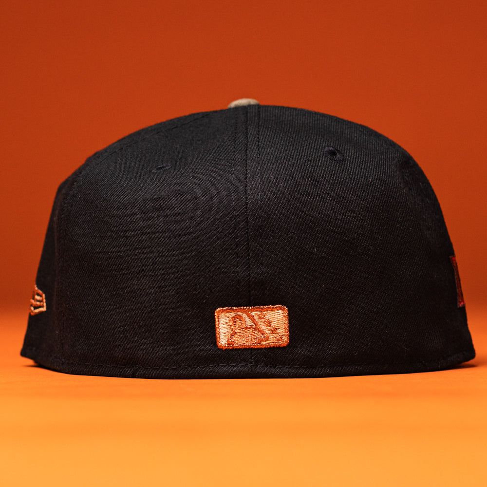 The Hooked in Camo Corpus Christi Hooks New Era Hat 5950 Fitted is shown backwards on an orange surface, featuring a small orange and white patch logo centered above the brim. The monochromatic image has an orange background that matches the surface.