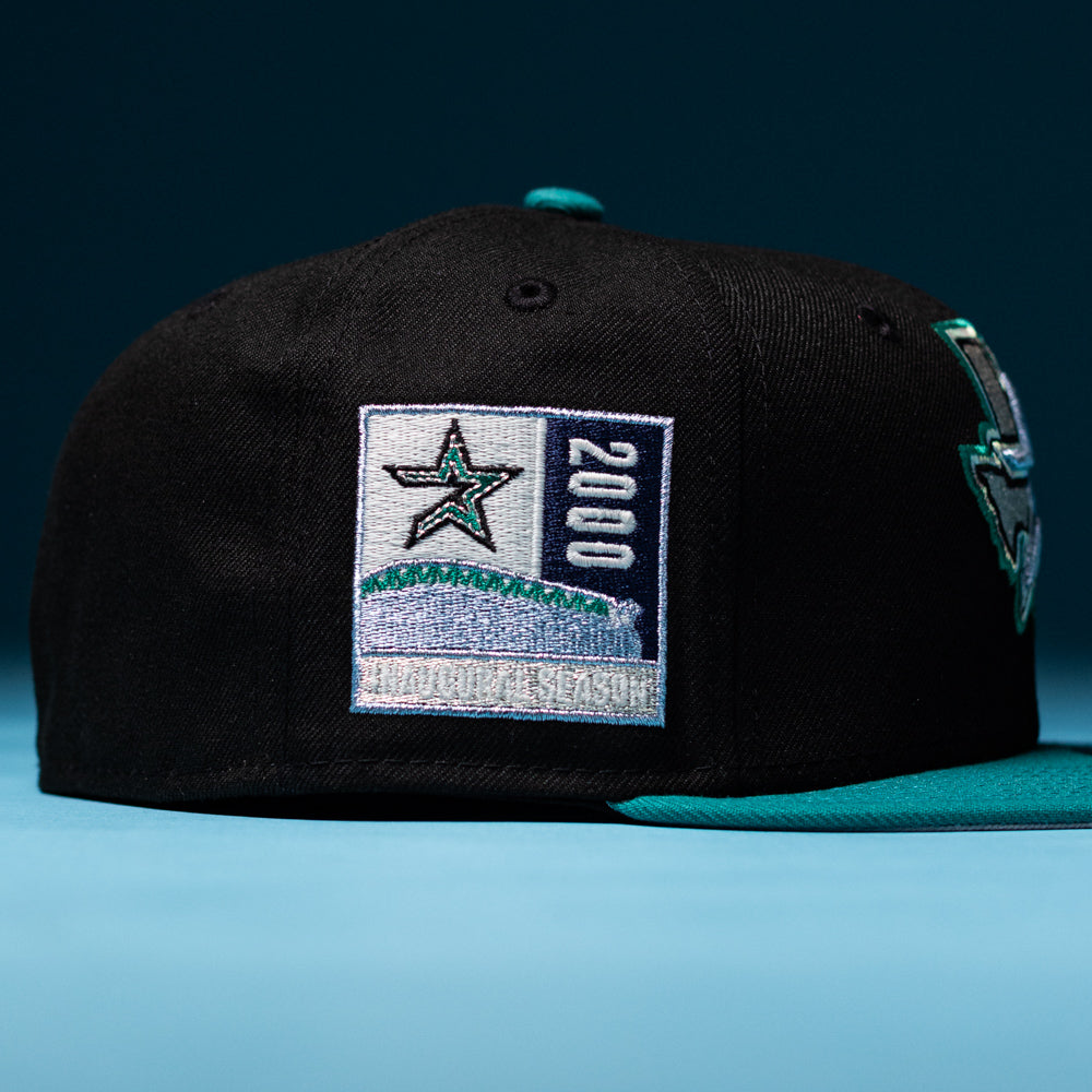 Introducing the Silver Lining Black Teal 2000 Houston Astros New Era Hat 5950 Fitted—a stylish fitted cap featuring bold black and teal hues, a striking star patch with “2000 INAUGURAL SEASON” embroidered on the side in eye-catching Chrome Black accents, all set against a vibrant blue background.