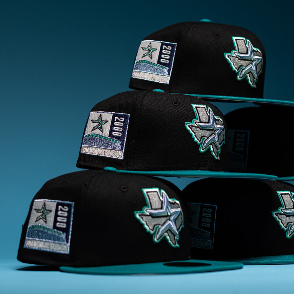 Four Silver Lining Black Teal 2000 Houston Astros New Era Hat 5950 Fitted caps are stacked, each showcasing a chrome black Texas state outline, a star, and a 2000 patch on the side—paying tribute to the Houston Astros. The background features a blue gradient.