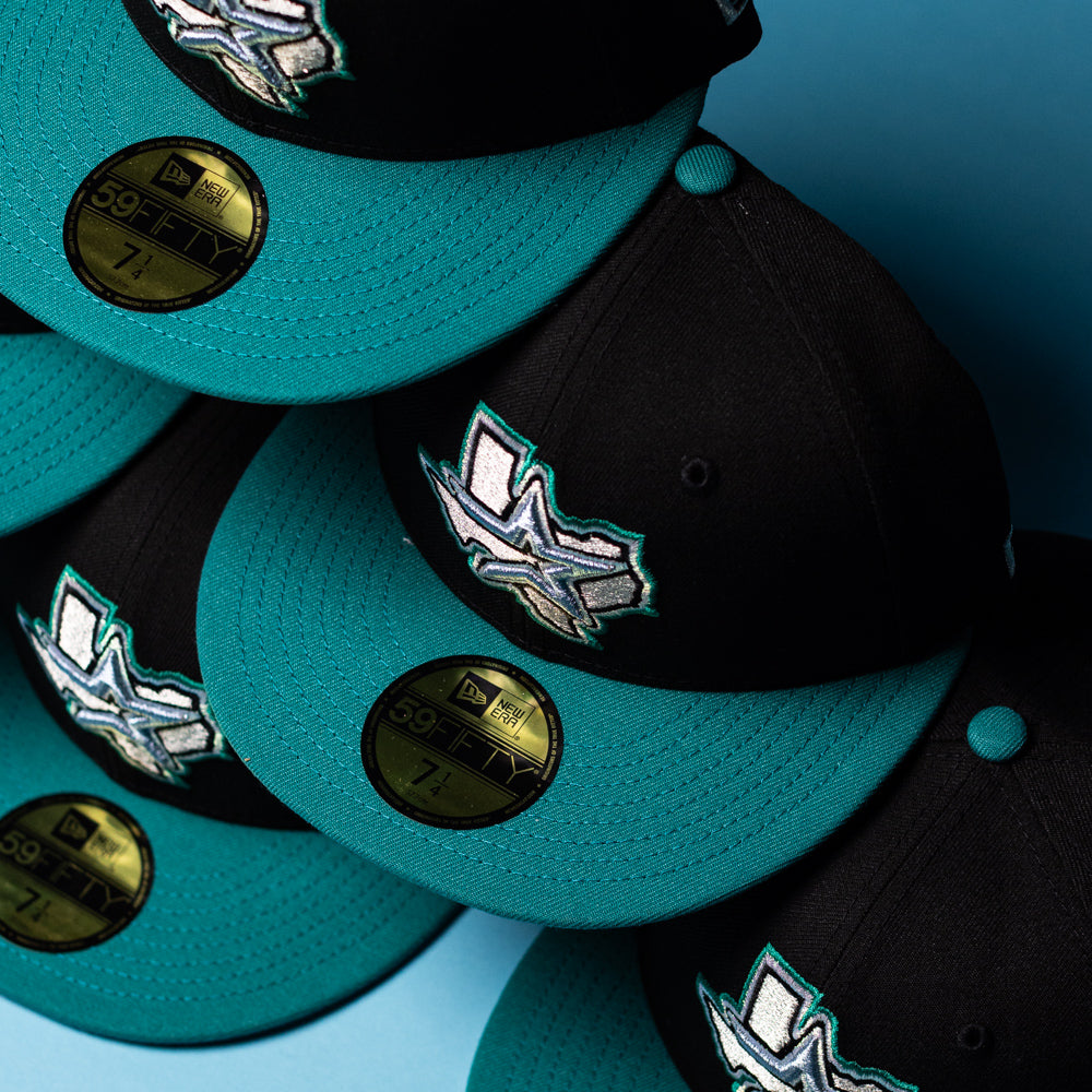 Five black and teal Silver Lining 2000 Houston Astros New Era 59FIFTY fitted hats are arranged in a diagonal pattern on a blue background. Each hat features gold sizing stickers on the brim and bold Chrome Black accents, highlighting the standout design of these Silver Lining Black Teal Houston Astros caps.