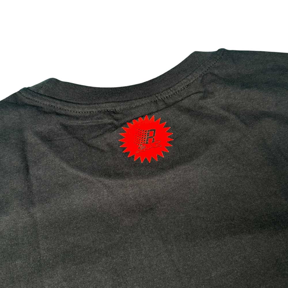 A close-up of the back neck on the Bronze 56K x Ice Cream Wunning Dog Tee Black displays a small red starburst graphic with an "R" and text printed directly on the fabric.