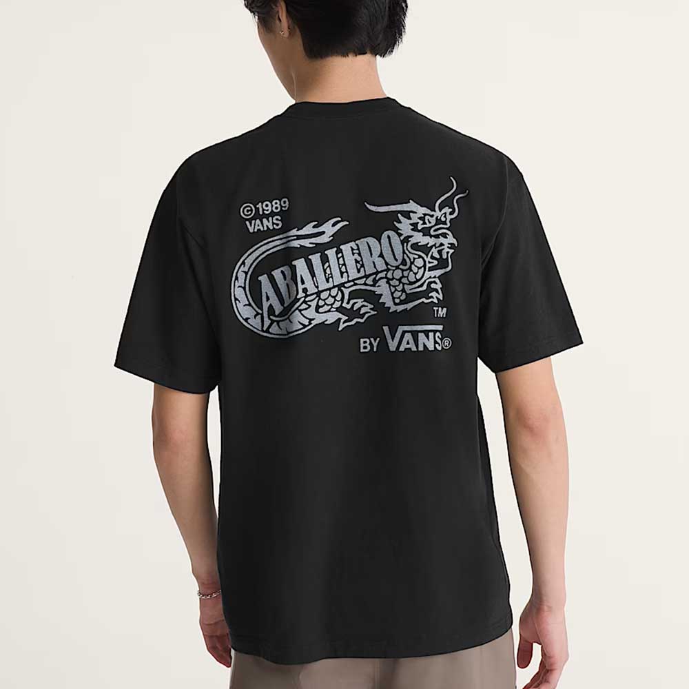 Someone wears a loose-fit Caballero VN000XHBBLK1 Black Short Sleeve Tee from Vans Skateboarding, featuring a bold dragon graphic and "CABALLERO" with BY VANS, VANS, and ©1989 VANS in white text on the back.
