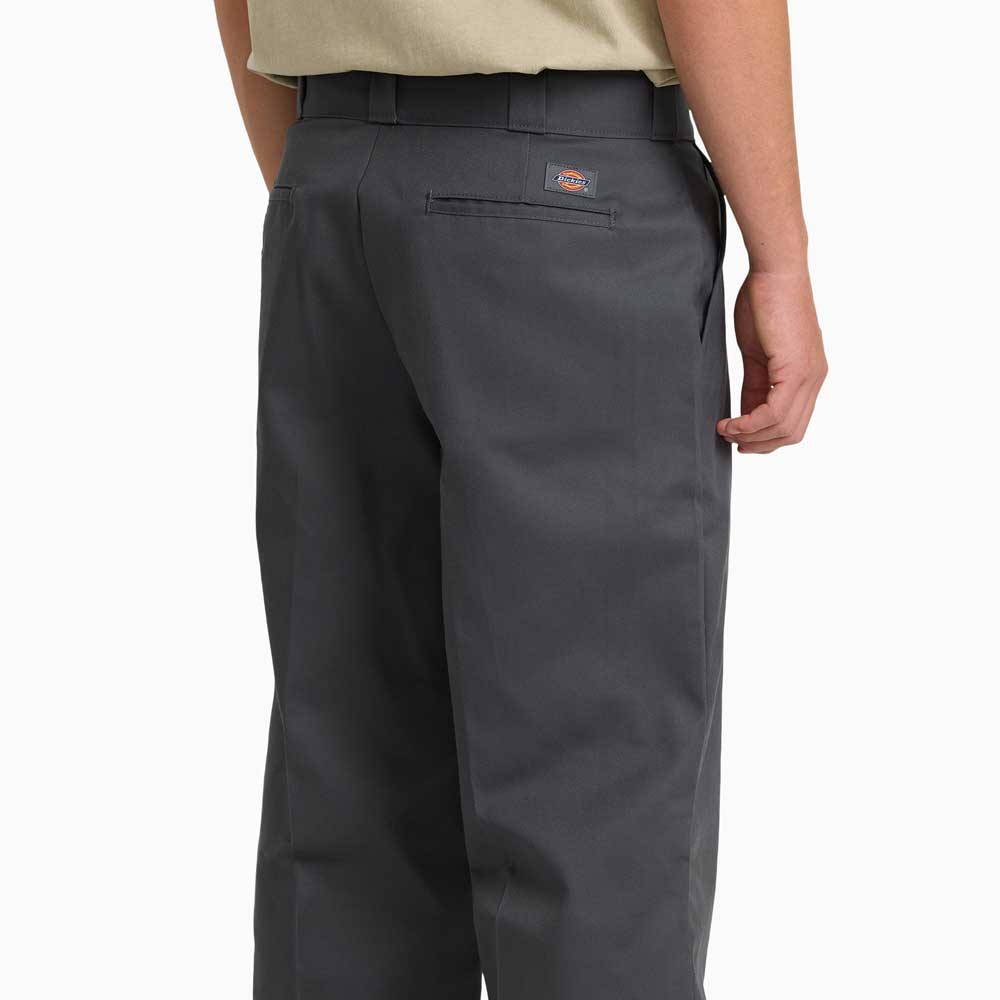 A person wearing Charcoal Loose Fit Work Pant A88KB0CH Dickies Skateboarding and a light beige shirt, viewed from the back. The pants feature durable twill, belt loops, welt back pocket, and a Dickies logo patch above the pocket.