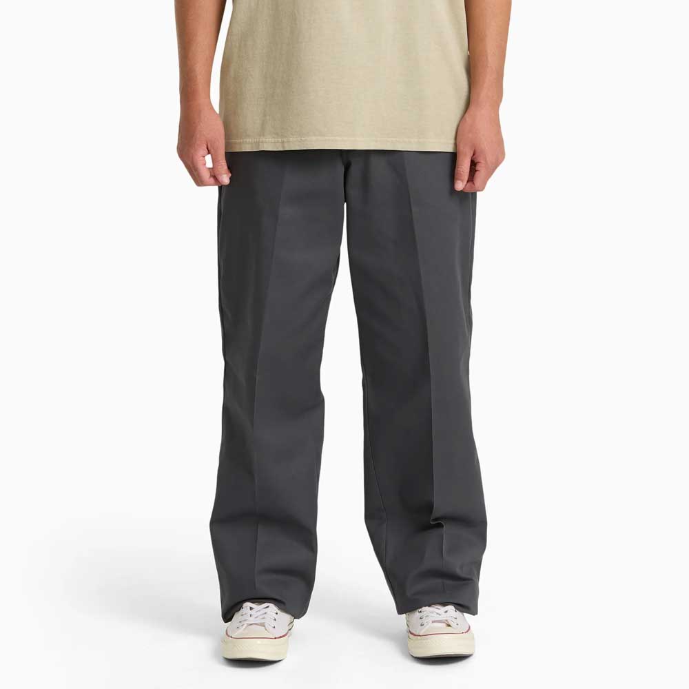 A person wearing a beige T-shirt, Charcoal Loose Fit Work Pant A88KB0CH Dickies Skateboarding, and white sneakers stands against a plain white background. The person's face is not visible.