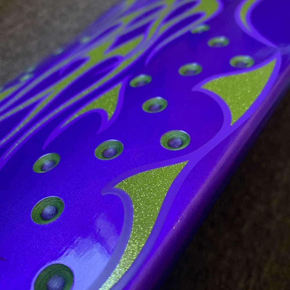 Close-up of a shiny surface with metallic purple and green patterns—curved lines and circular dots—evoking the graphics on the Chop Shop Flame 8.50in x 32.05in Creature Skateboard Shaped Deck made from 7 ply North American Maple. Softly blurred background.