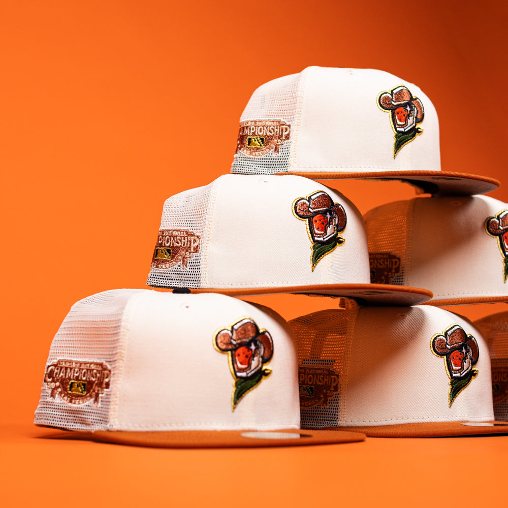 Six white The Wrangler Chrome Rust Sugarland Space Cowboys New Era Hat 5950 Fitted trucker hats with brown brims are stacked against an orange background, each featuring a cartoon monkey logo and a CHAMPIONSHIP patch on the side, capturing the playful spirit of Space Cowboys Hat designs reminiscent of the Chrome Rust Champ 24 series.