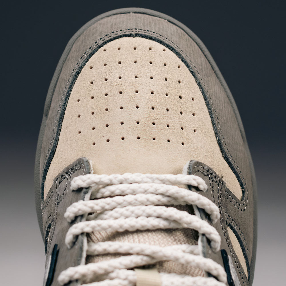 Close-up of the toe area of the 480 CVL New Balance Numeric x Civil Suede Leather Skateboarding Shoe, showcasing its durable beige suede construction with gray accents. The shoe features perforations on the toe box, an ABZORB midsole for added comfort, and white braided laces.