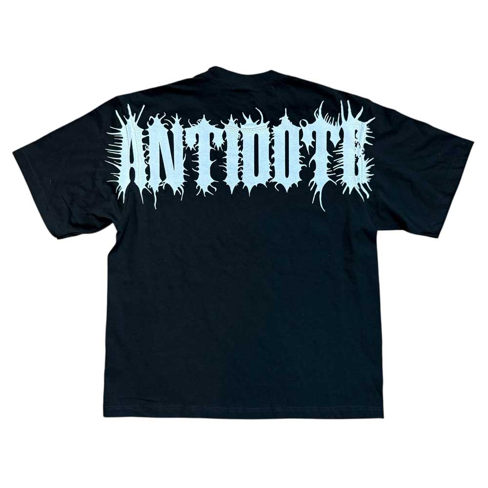 The Cropped White Shoulder Antidote Black Tee is an oversized black shirt with bold, spiky ANTIDOTE lettering on the back. Made from 100% USA cotton, it offers a striking, streetwear-inspired edge.
