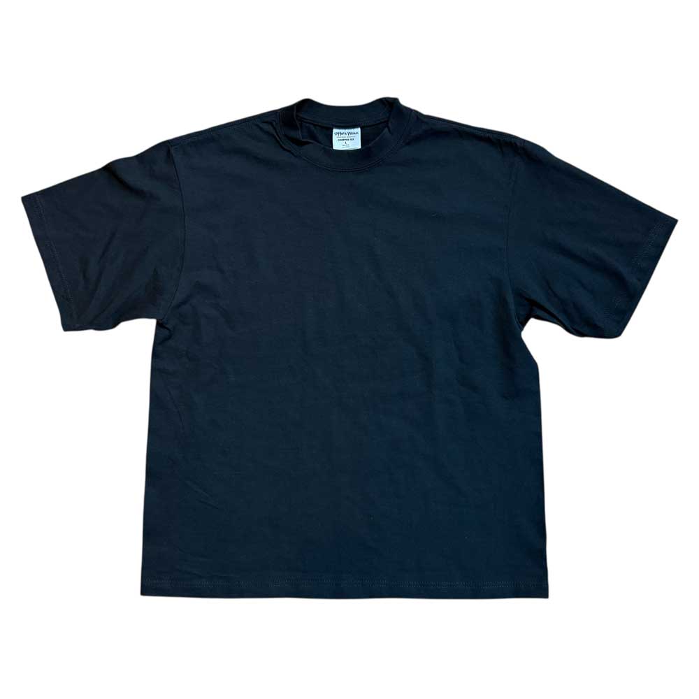 The Cropped White Shoulder Antidote Black Tee, made from 100% USA cotton, is a plain black short-sleeve shirt laid flat on a white background with its neck tag visible by the collar.