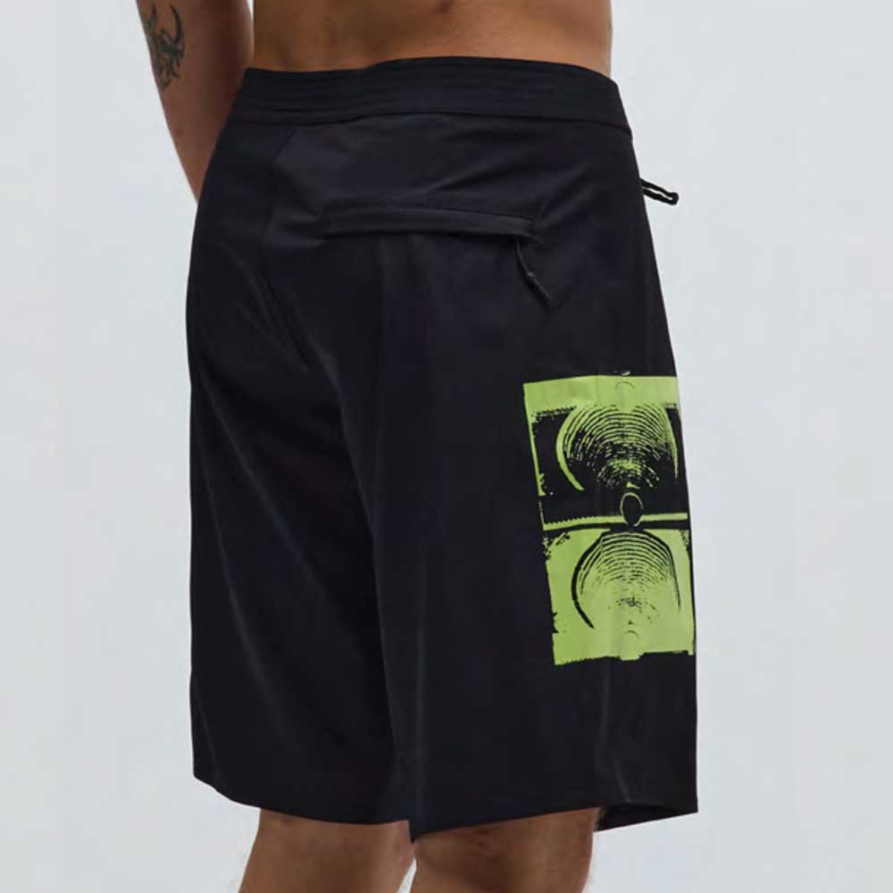 A person wearing the Illusion 21 inch Trunk Black Former, which features a green graphic of audio speakers on the side, standing against a plain light background.
