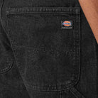 Close-up of the back pocket on DDSK68 Loose Fit Denim Pant Carpenter Black Dickies Skateboarding jeans, showing a small rectangular Dickies Skateboarding label stitched on the pocket. Part of a person’s arm appears on the right.