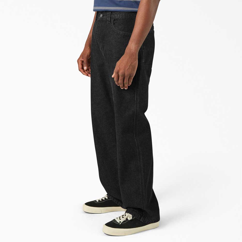 A person wearing DDSK68 Loose Fit Denim Pant Carpenter Black Dickies Skateboarding jeans, a blue-striped t-shirt, and black-and-white sneakers stands against a plain white background.