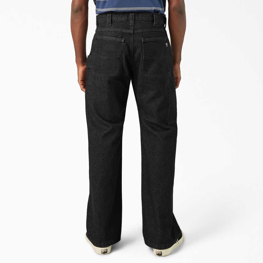 A person is shown from the back in DDSK68 Loose Fit Denim Pant Carpenter Black by Dickies Skateboarding, featuring large rear pockets and visible seam details, paired with white sneakers against a plain white background.