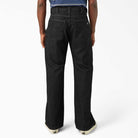 A person is shown from the back in DDSK68 Loose Fit Denim Pant Carpenter Black by Dickies Skateboarding, featuring large rear pockets and visible seam details, paired with white sneakers against a plain white background.