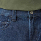 Close-up of a person wearing DDSK68 Loose Fit Denim Pant Carpenter Dark Wash Dickies Skateboarding jeans with front pocket, belt loop, and metal button, paired with an olive green shirt tucked in at the waist.