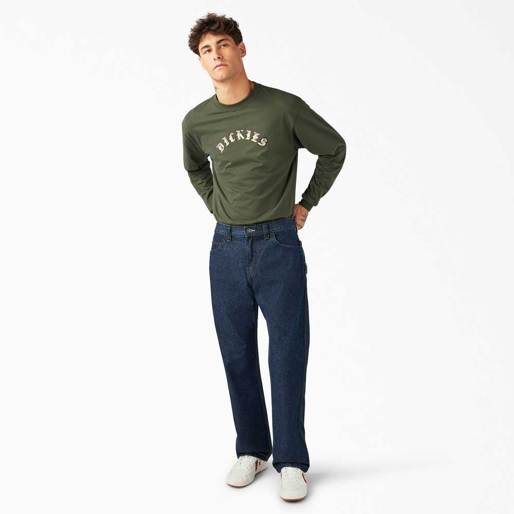 A young man stands against a white background in a green long-sleeve shirt, DDSK68 Loose Fit Denim Pant Carpenter Dark Wash by Dickies Skateboarding, and white sneakers. He has short, tousled hair and poses casually with his hands in his pockets.