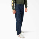 A person wearing DDSK68 Loose Fit Denim Pant Carpenter Dark Wash Dickies Skateboarding jeans, a green long-sleeve shirt with a flame sleeve design, and white sneakers with red accents stands against a plain white background.