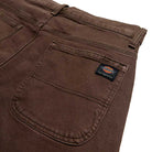 Close-up of DDSK68J84 Loose Fit Denim Pant in Wingville Brown Tint Wash by Dickies Skateboarding, highlighting the back pocket with sewn-on logo, detailed stitching, part of the waistband, and a belt loop.
