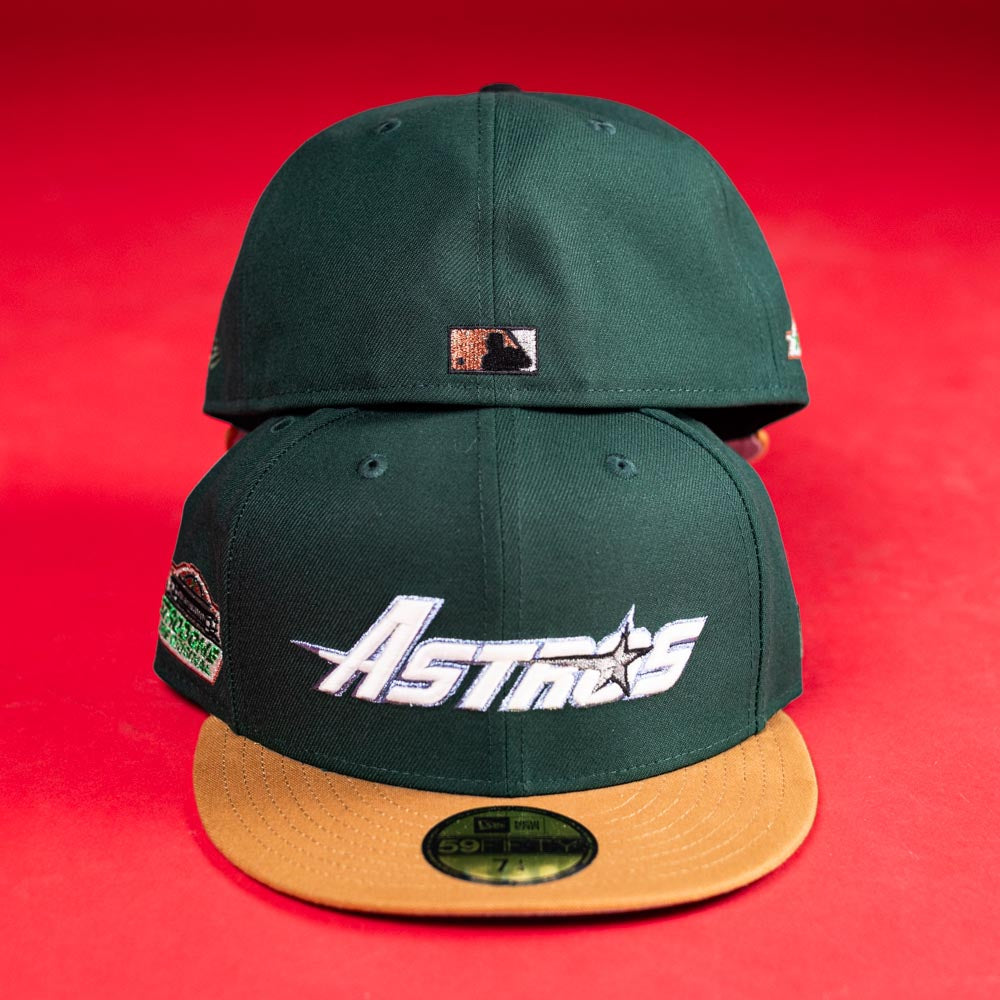 Two El Tuga Houston Astros New Era 5950 Fitted hats in dark green with tan brims are shown on a red surface. The front hat displays the Astros logo; the back shows a small MLB logo. Great for any fan or fishing pack.