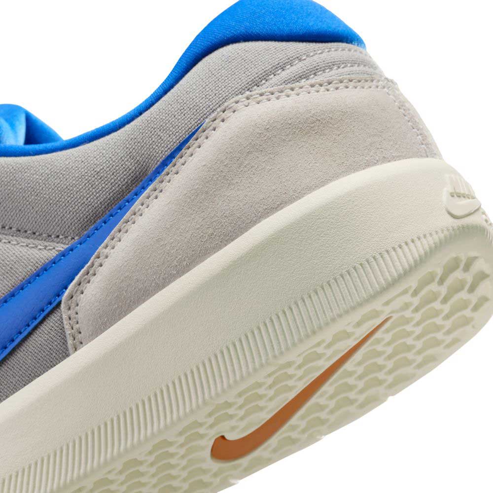 Close-up of the heel and sole of the DV5477-011 College Grey/Racer Blue/Light Orewood Nike SB Force 58 suede skateboarding shoes, showing light grey suede, blue accents, an orange Swoosh, and a textured off-white sole with modern cupsole design.