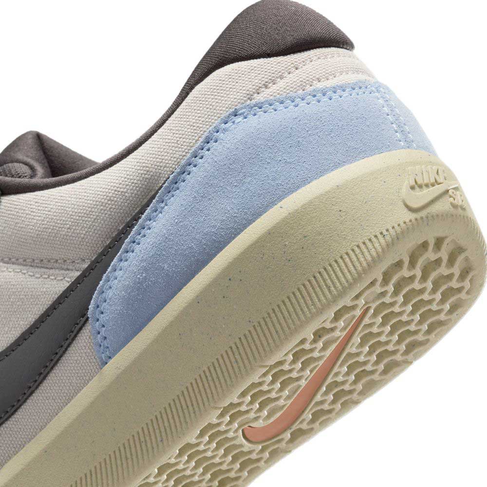 Close-up of the heel of the DV5477102 Light Orewood Brown Medium Aah Force 58 Nike SB suede skateboarding shoes, showing a pale blue suede panel, light beige textured cupsole, black Nike swoosh, and light gray fabric upper.