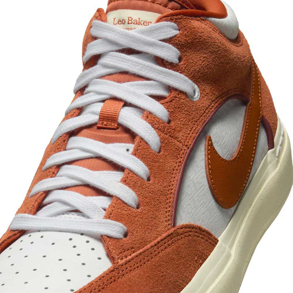 A close-up of the Nike SB DX4361-202 Dark Rust White React Leo skate shoe in orange and white suede and leather. The tongue features Leo Baker's name in orange, highlighting this collaboration, with a bold orange Swoosh on the side.