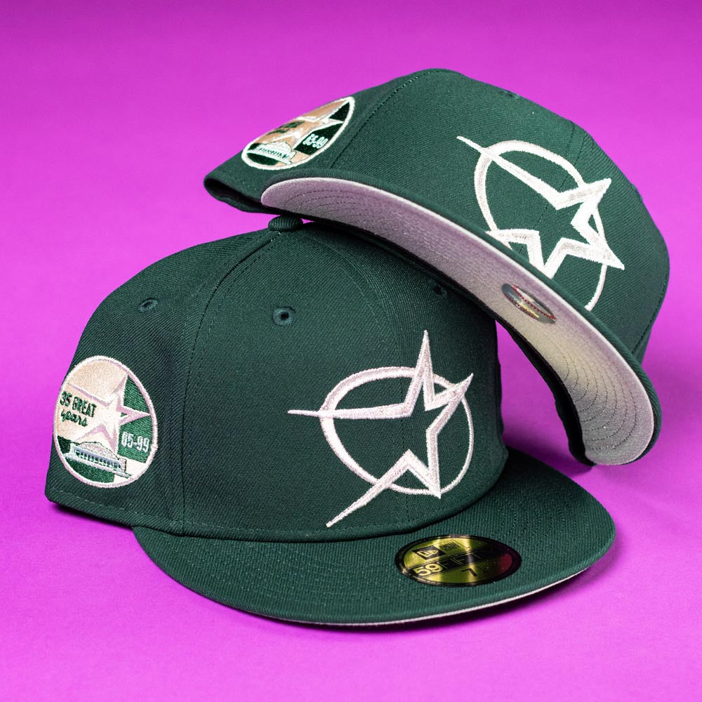 Two Merc Green Silver 35th Houston Astros New Era 5950 Fitted hats with white star logos and multiple patches are displayed on a bright purple background. One is upright, the other tilted to show the underside of the brim.
