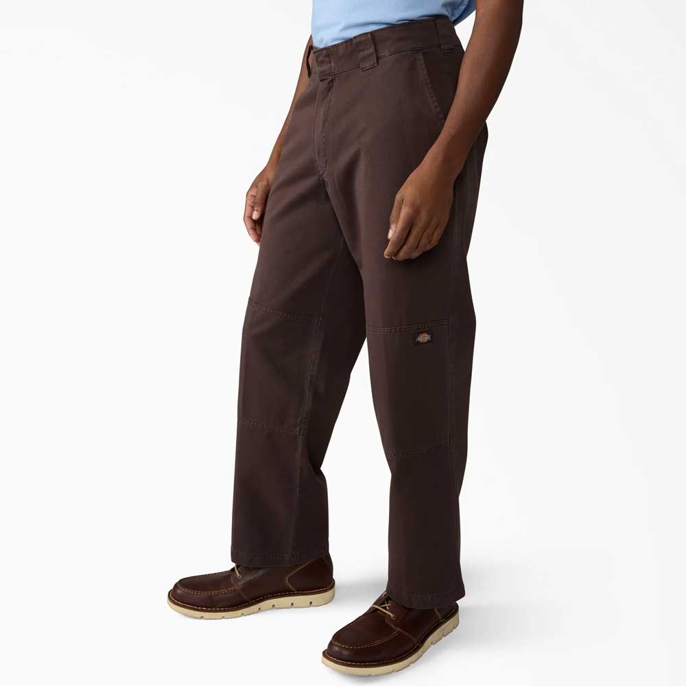 Person wearing Dark Brown Worn In Double Knee Pant A89TC0DB Dickies Skateboarding, a light blue shirt, and brown lace-up shoes stands against a white background. The loose fit pants feature reinforced double knees for extra durability.
