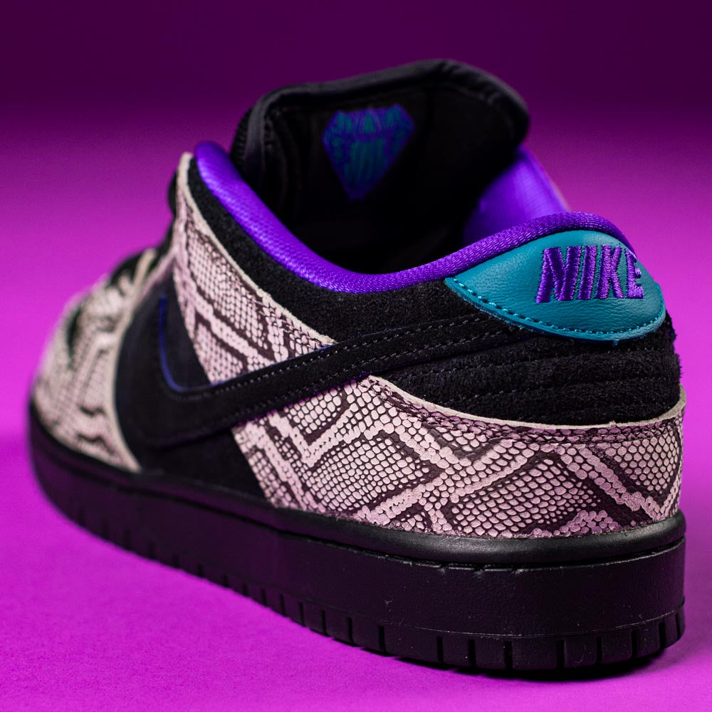 A close-up of the READ BELOW the BUTTON RAFFLE Nike SB Dashawn Jordan Dunk Low pops against a vibrant purple background—featuring snakeskin pattern, black suede, teal heel tab, and purple trim for your Southside Skatepark raffle entry.