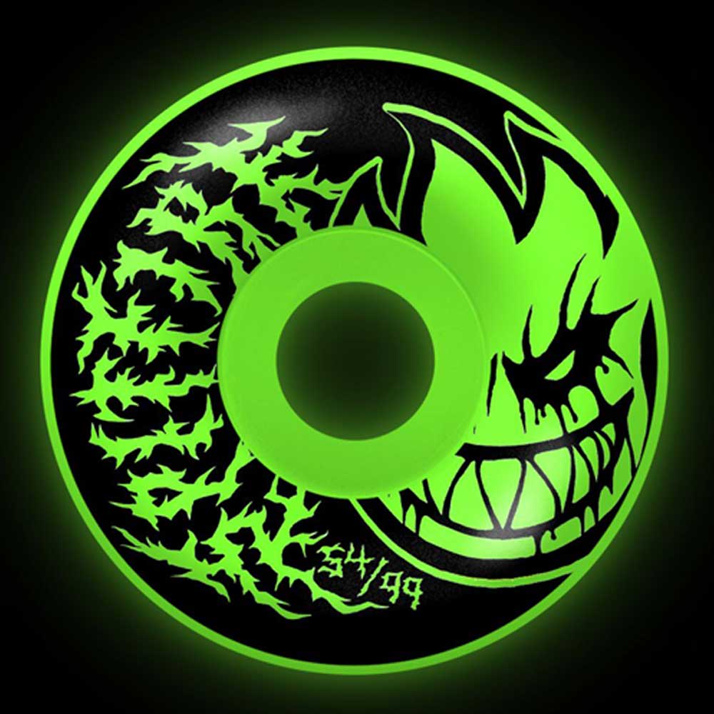 A neon green Deathmask II Radial Full Glow 54mm 99A Formula Four Spitfire Wheels set, shown against black, features a grinning flame-face and jagged design with "54/99" marking near the bottom edge.
