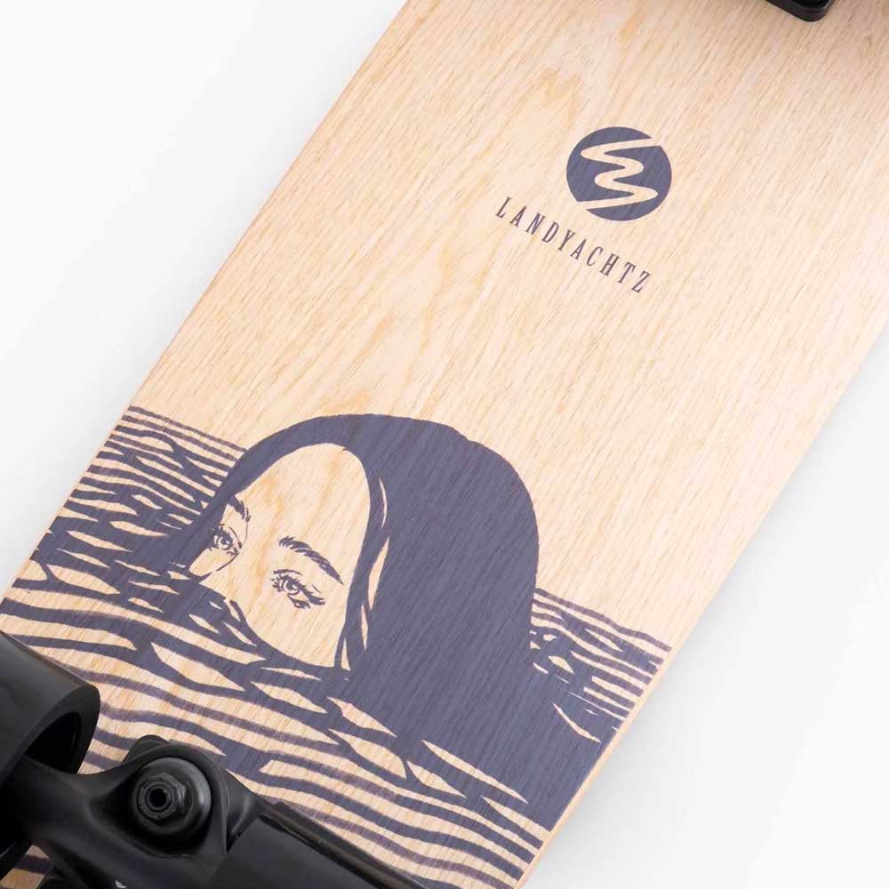 Close-up of a Dinghy Classic Fender Moray Eel Landyachtz Complete Skateboard featuring an illustrated woman's face in stylized waves, molded wheel flares, and the LANDYACHTZ logo on a wood grain background.