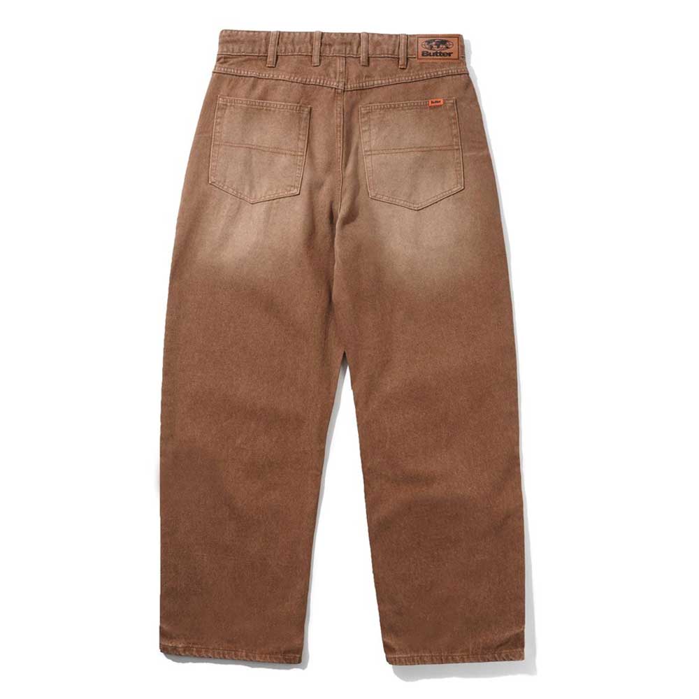 Distressed Brown Relaxed Denim Jeans from Butter Goods, shown from the back, feature two rear pockets, belt loops, a leather patch on the waistband, and a relaxed fit straight-leg silhouette with subtle fading. 100% cotton.