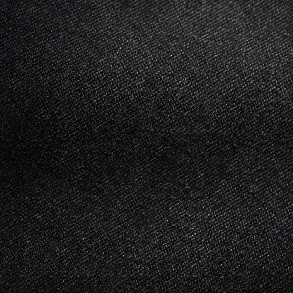 Close-up of Distressed Flat Black Relaxed Denim Jeans by Butter Goods, featuring 100% cotton fabric with a diagonal weave and textured surface, highlighted by subtle shadows.