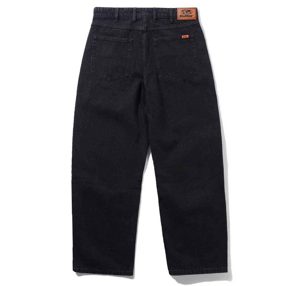 The Distressed Flat Black Relaxed Denim Jeans by Butter Goods are 100% cotton with a straight leg cut, visible stitching, two back pockets, a brown leather waistband patch, and a comfortable relaxed fit.