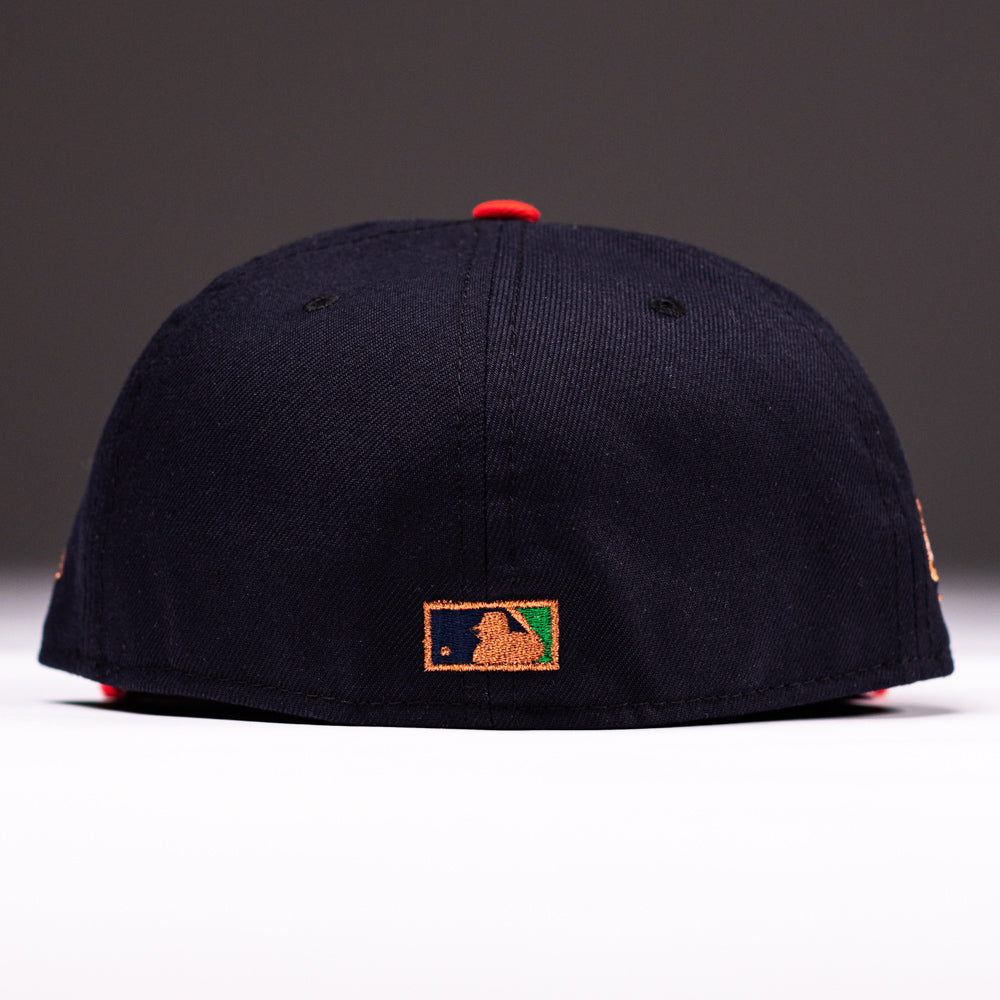 A black El Karma ASG Navy Red Houston Astros New Era Hat 5950 Fitted is viewed from the back, featuring the MLB logo embroidered in gold, green, and white on the bottom center. The background is plain and softly lit—perfect for any Astros fan seeking a stylish finishing touch.